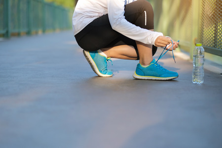 Young athlete woman tying running shoes in the park outdoor, female runner ready for jogging on the road outside, asian Fitness walking and exercise on footpath in morning. wellness and sport conceptsの写真素材
