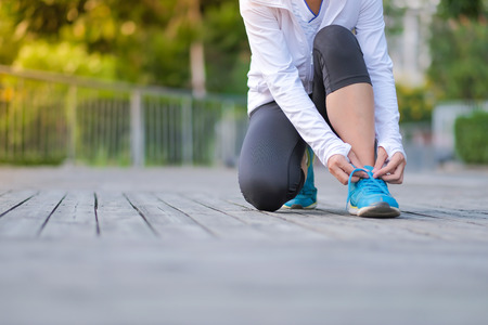 Young athlete woman tying running shoes in the park outdoor, female runner ready for jogging on the road outside, asian Fitness walking and exercise on footpath in morning. wellness and sport conceptsの写真素材