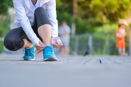 Young athlete woman tying running shoes in the park outdoor, female runner ready for jogging on the road outside, asian Fitness walking and exercise on footpath in morning. wellness and sport conceptsの写真素材