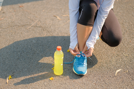 Young athlete woman tying running shoes in the park outdoor, female runner ready for jogging on the road outside, asian Fitness walking and exercise on footpath in morning. wellness and sport conceptsの写真素材