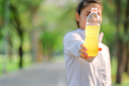 young fitness woman drinking energy water during walking in the park outdoor, female runner running on the road outside, asian athlete jogging and exercise on footpath in morning.Sport and wellness conceptの写真素材