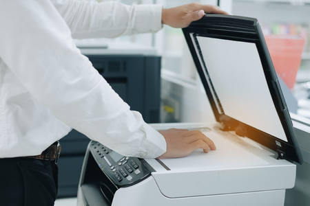 Bussiness man Hand putting a document paper into printer scanner or laser copy machine in officeの写真素材