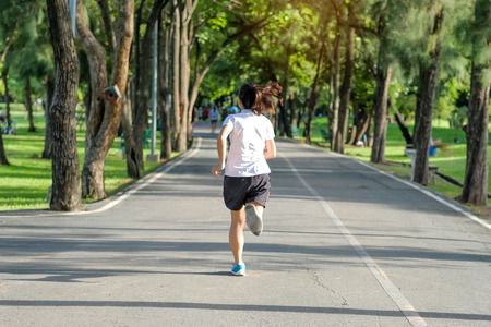 young fitness woman running in the park outdoor, female runner walking on the road outside, asian athlete jogging and exercise on footpath in sunlight morning. Sport, healthy and wellness conceptsの写真素材