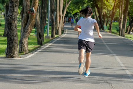 young fitness woman running in the park outdoor, female runner walking on the road outside, asian athlete jogging and exercise on footpath in sunlight morning. Sport, healthy and wellness conceptsの写真素材