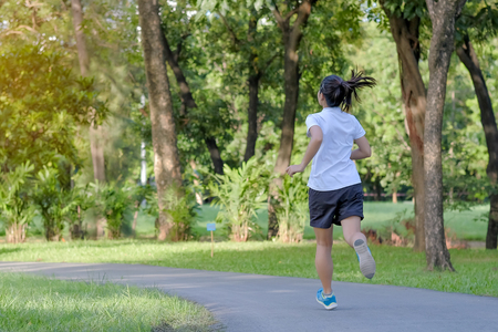 young fitness woman running in the park outdoor, female runner walking on the road outside, asian athlete jogging and exercise on footpath in sunlight morning. Sport, healthy and wellness conceptsの写真素材