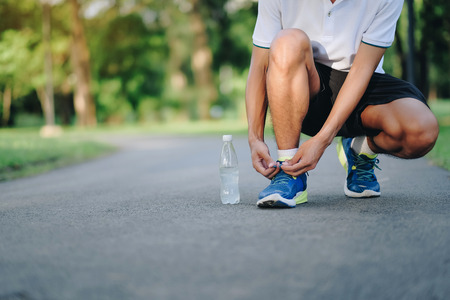 Young athlete man tying running shoes in the park outdoor, male runner ready for jogging on the road outside, asian Fitness walking and exercise on footpath in morning. wellness and sport conceptsの写真素材