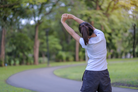 Young athlete woman streching in the park outdoor, female runner warm up ready for jogging on the road outside, asian Fitness walking and exercise on footpath in morning. wellness and sport conceptsの写真素材
