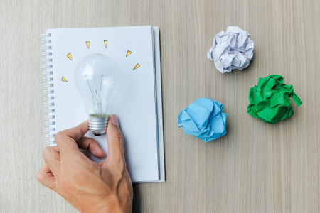 Hand holding light bulb or lamp with colorful crumpled paper on wooden table. New Idea, Creative, Genius and Innovation conceptsの写真素材