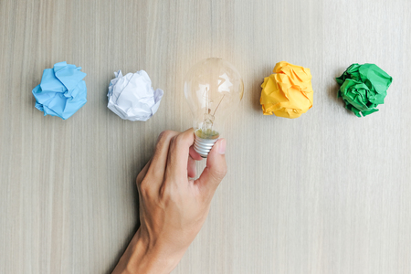 Hand holding light bulb or lamp with colorful crumpled paper on wooden table. New Idea, Creative, Genius and Innovation conceptsの写真素材