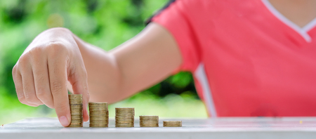 Woman hand putting coin, gold coins stack on wooden table in the morning sunlight. business,...