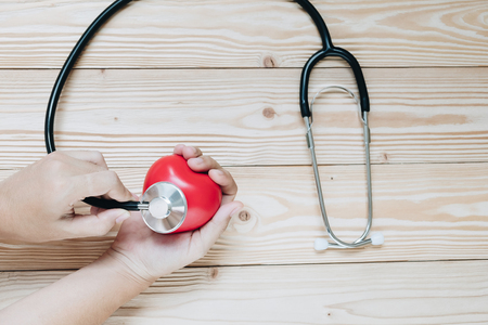 hand holding Stethoscope with Red heart shape on wooden background. Healthcare and Insurance conceptの写真素材