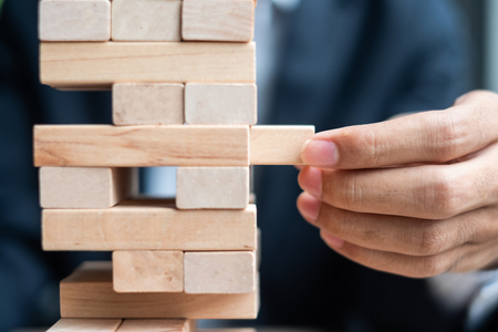 Businessman hand placing or pulling wooden block on the tower. Business planning, Risk Management, Solution and strategy Conceptsの写真素材
