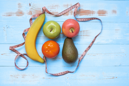 Measuring tape, banana, apple avocado and orange  on blue  wooden background. Healthcare and healthy food concept, Top view and Copy space for your textの写真素材