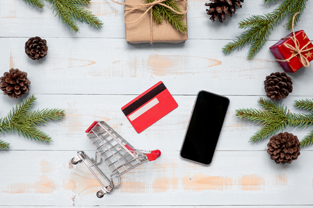 Shopping cart, smart phone, credit card  with Christmas decoration, gift box and pine tree branches on wooden background. E-commerce purchase and preparation for Happy New Year and Xmas Holidays.の写真素材