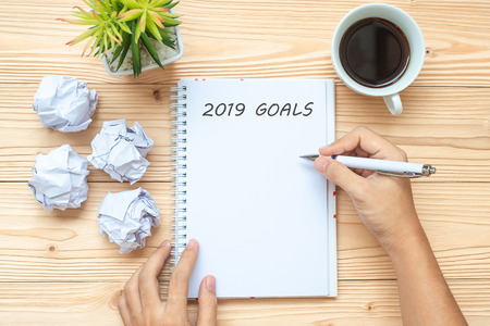 Businesswoman writing 2019 Goals with notebook, crumbled paper and black coffee cup on table. New Year Start, Creative, Idea, Resolution, Solution, Strategy and Mission conceptの写真素材