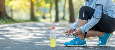 Young athlete woman tying running shoes in the park outdoor, female runner ready for jogging on the road outside, asian Fitness walking and exercise on footpath in morning. wellness and sport conceptsの写真素材
