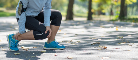 Young fitness woman holding his sports leg injury, muscle painful during training. Asian runner having calf ache and problem after running and exercise outside in summerの写真素材