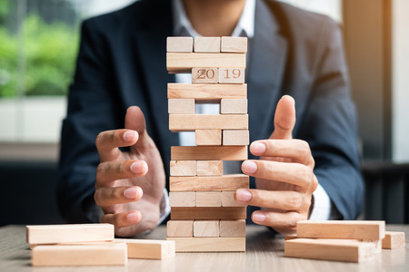 Businessman hand placing or pulling wooden block on the tower. Business planning, Risk Management, Solution and strategy Conceptsの写真素材