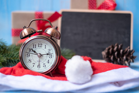 Retro alarm clock with Merry Christmas gift box or Present and Santa Claus hat on blue wooden...