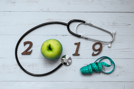 2019 Happy New Year for healthcare, Wellness and medical concept. Stethoscope with green apple, measuring tape and wooden number on table backgroundの写真素材