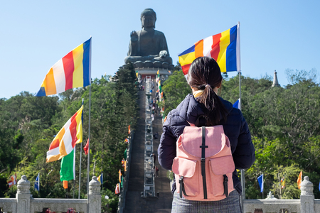 Young woman traveling backpacker, Asian traveler visit the Tian Tan or Big Buddha located at Po Lin Monastery in Ngong Ping Lantau Island. landmark and popular for tourist attractions in Hong Kongの写真素材