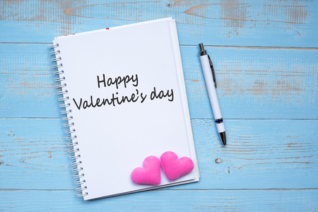 HAPPY VALENTINE'S DAY word on notebook and pen with couple pink heart shape decoration on blue wooden table background. Wedding, Romantic and holiday conceptの写真素材
