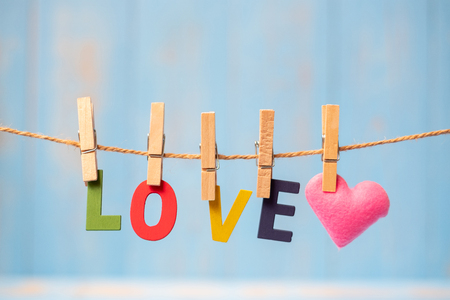 LOVE text and pink heart shape decoration hanging on line with copy space for text on blue wooden background. Love, Wedding, Romantic and Happy Valentineâ s day holiday conceptの写真素材
