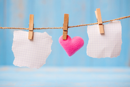blank paper and pink heart shape decoration hanging on line with copy space for text on blue wooden background. Love, Wedding, Romantic and Happy Valentineâ s day holiday conceptの写真素材
