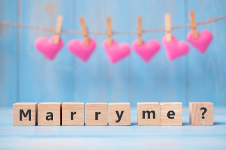 MARRY ME? wooden cubes with pink heart shape decoration on blue table background and copy space for text. Love, Romantic and Happy Valentineâs day holiday conceptの写真素材