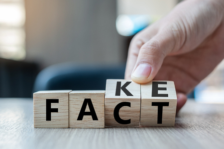 Business man hand holding wooden cube with flip over block FAKE to FACT word on table background. News, solution and business  conceptsの写真素材