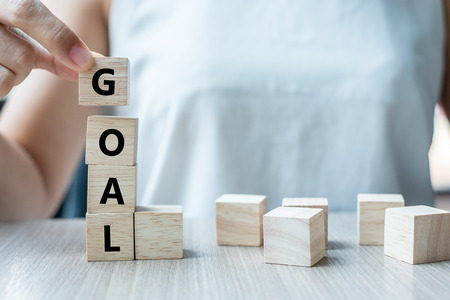 Businesswoman hand holding wooden cube with GOAL text on table background. success, strategy, solution and business conceptsの写真素材