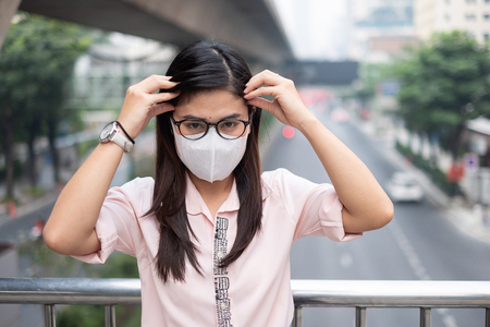 young Asian woman wearing N95 respiratory mask protect and filter pm2.5 (particulate matter) against traffic and dust city. healthcare and air pollution conceptの写真素材