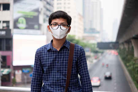 young Asian man wearing N95 respiratory mask protect and filter pm2.5 (particulate matter) against traffic and dust city. healthcare and air pollution conceptの写真素材