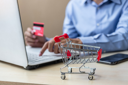 close up mini cart, Asian businessman holding credit card and using laptop for online shopping while making orders. internet, technology, ecommerce and online payment conceptの写真素材