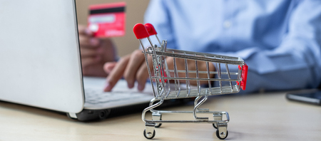 close up mini cart, Asian businessman holding credit card and using laptop for online shopping while making orders. internet, technology, ecommerce and online payment conceptの写真素材