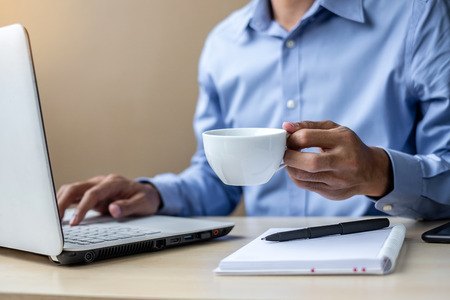 young Businessman using laptop analysis marketing plan and drinking coffee in the morning. Business, Finance and lifestyle conceptsの写真素材