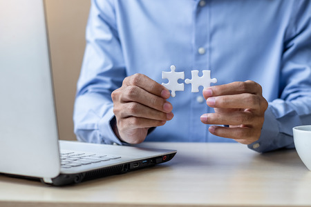 Businessman Hand connecting couple puzzle piece in office. Business solutions, mission, successful, goals and strategy conceptsの写真素材