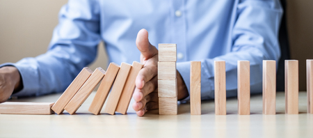 Businessman hand Stopping Falling wooden Blocks or Dominoes. Business, Risk Management, Solution, Insurance and strategy Conceptsの写真素材