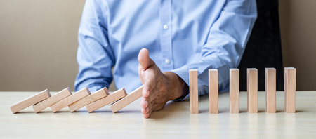 Businessman hand Stopping Falling wooden Blocks or Dominoes. Business, Risk Management, Solution, Insurance and strategy Conceptsの写真素材