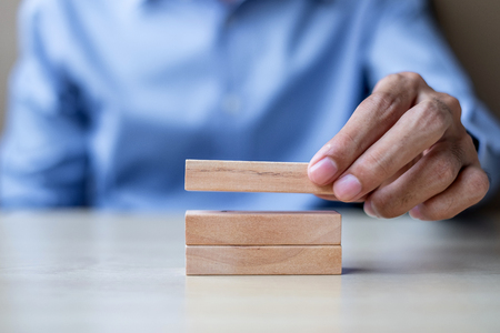 Businessman hand holding wooden building blocks on table background. Business planning, Risk Management, Solution and strategy Conceptsの写真素材