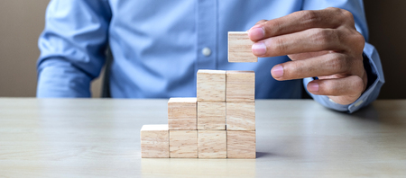 Businessman hand placing or pulling wooden block on the building. Business planning, Risk Management, Solution and strategy Conceptsの写真素材