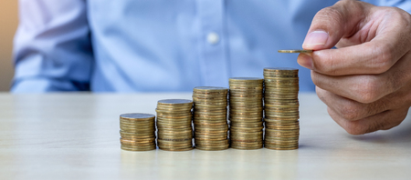 Businessman hand putting golden coin on growing money stairs or stack on wooden table. business, investment, retirement planning, finance and Saving for the future conceptsの写真素材