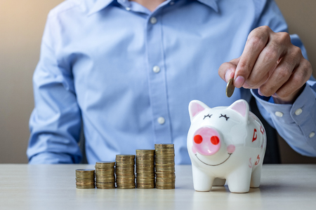 Businessman hand putting golden coin on piggy banking with growing money stairs or stack on wooden table. business, investment, retirement planning, finance and Saving for the future conceptsの写真素材