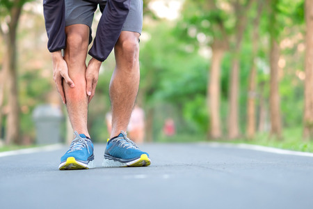 Young fitness man holding his sports leg injury. muscle painful during training. Asian runner having calf ache and problem after running and exercise outside morning. sport and healthy conceptsの写真素材