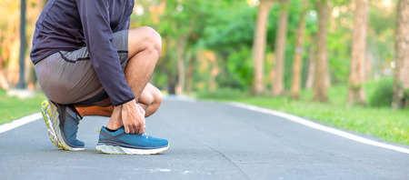 Young athlete man tying running shoes in the park outdoor, male runner ready for jogging on the road outside, asian Fitness walking and exercise on footpath in morning. wellness and sport conceptsの写真素材