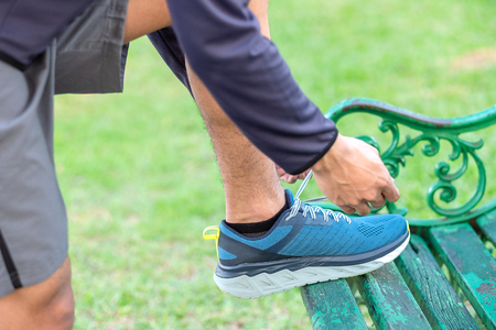 Young athlete man tying running shoes in the park outdoor, male runner ready for jogging on the road outside, asian Fitness walking and exercise on footpath in morning. wellness and sport conceptsの写真素材