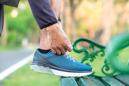 Young athlete man tying running shoes in the park outdoor, male runner ready for jogging on the road outside, asian Fitness walking and exercise on footpath in morning. wellness and sport conceptsの写真素材