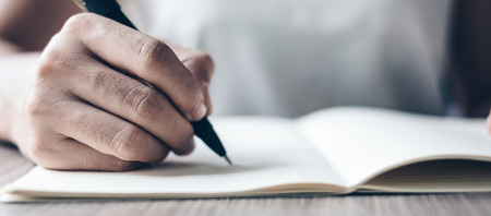 Businesswoman writing on notebook in office, hand of woman holding pen with signature on paper report. business conceptsの写真素材