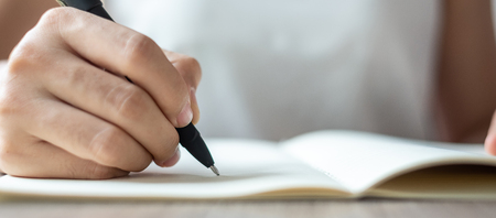 Businesswoman writing on notebook in office, hand of woman holding pen with signature on paper report. business conceptsの写真素材