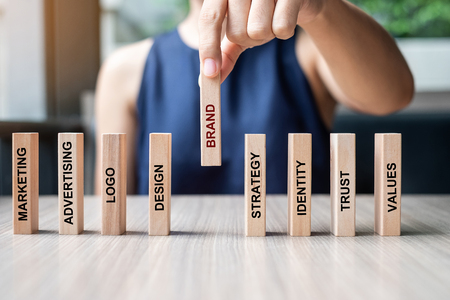 Businesswoman hand placing or pulling wooden Dominoes with BRAND text. and Marketing, Advertising, Logo, Design, Strategy, Identity, Trust and Values. Product development conceptの写真素材
